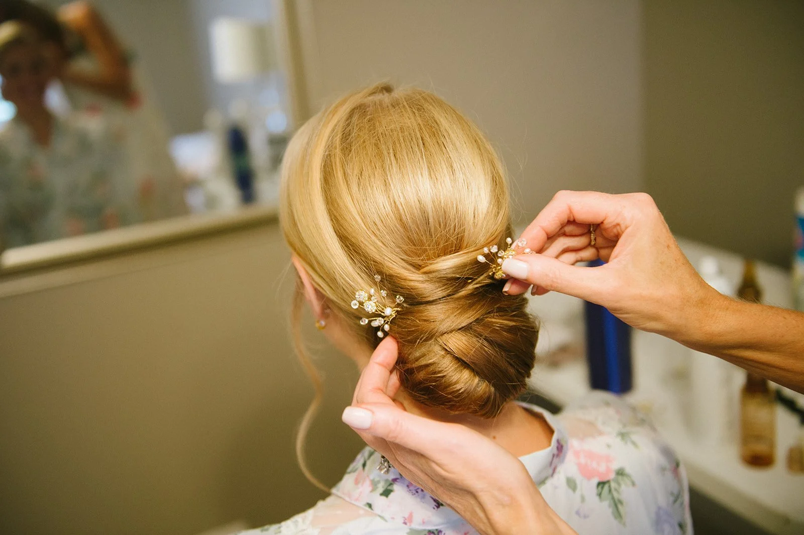 Stylist creating an elegant updo with decorative hairpins for a blonde woman in a mirrored salon room – bridal hair styling at One Salon & Bridal Co in St. Charles, IL