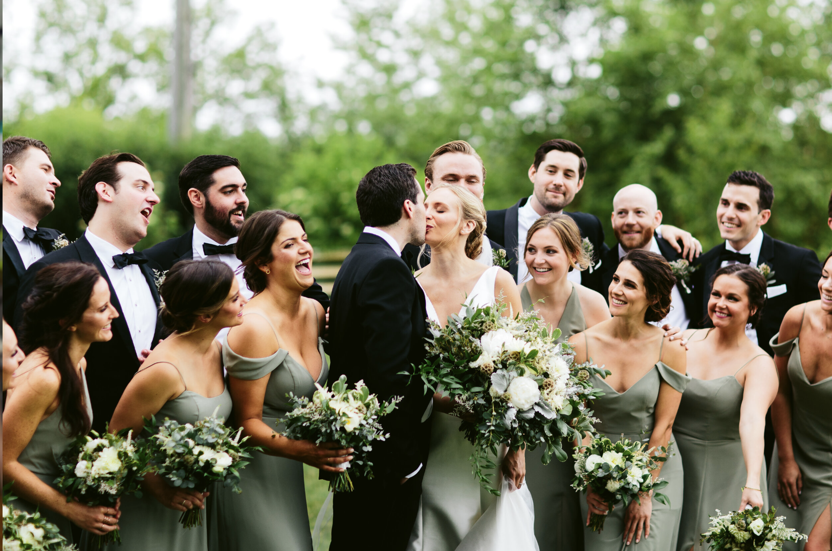 Bride and groom kissing surrounded by bridal party outdoors – styled by One Salon & Bridal Co in St. Charles, IL