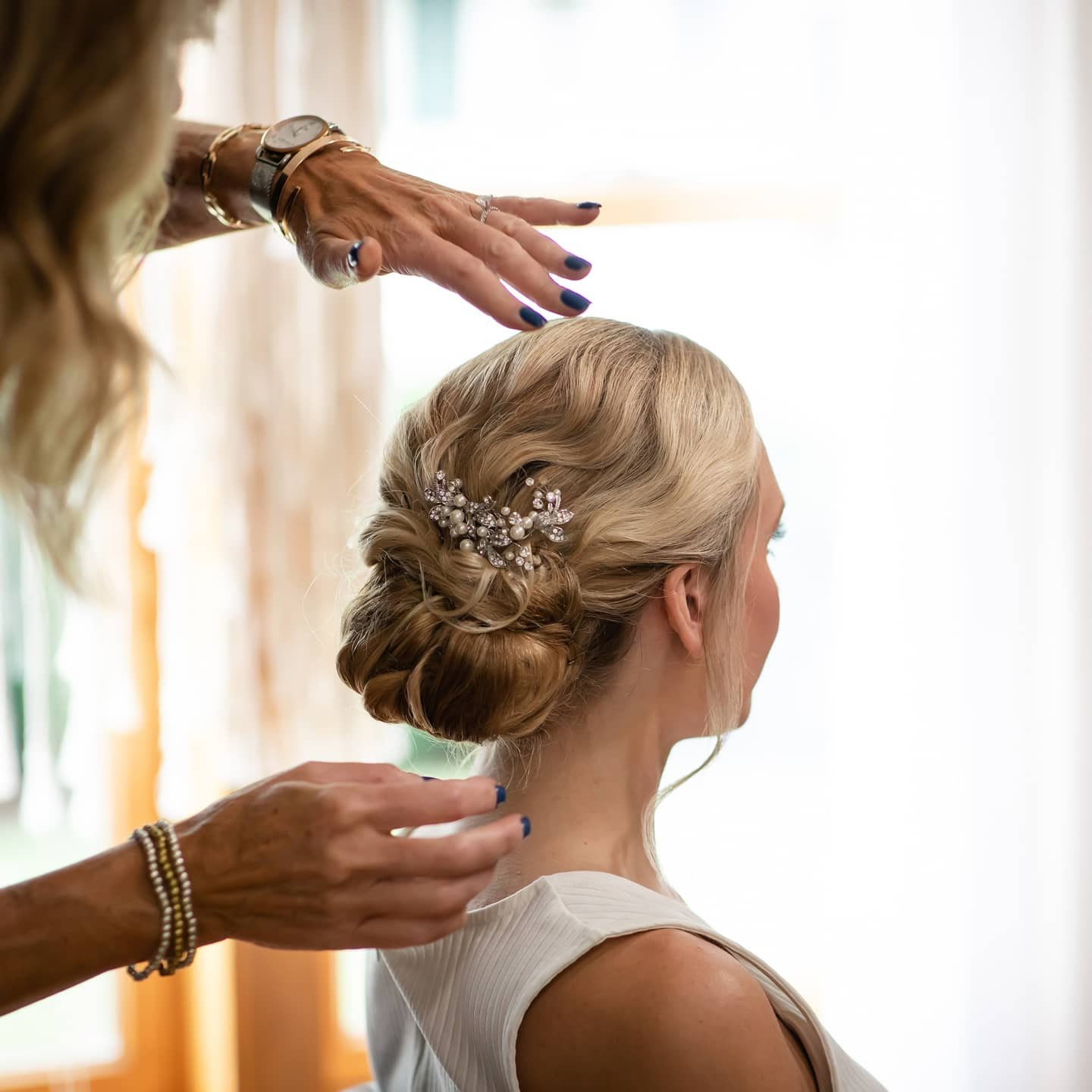 Woman with styled blonde hair adorned with a pearl and flower hairpiece being prepared by a stylist for a wedding or special occasion at One Salon & Bridal Co in St. Charles, IL
