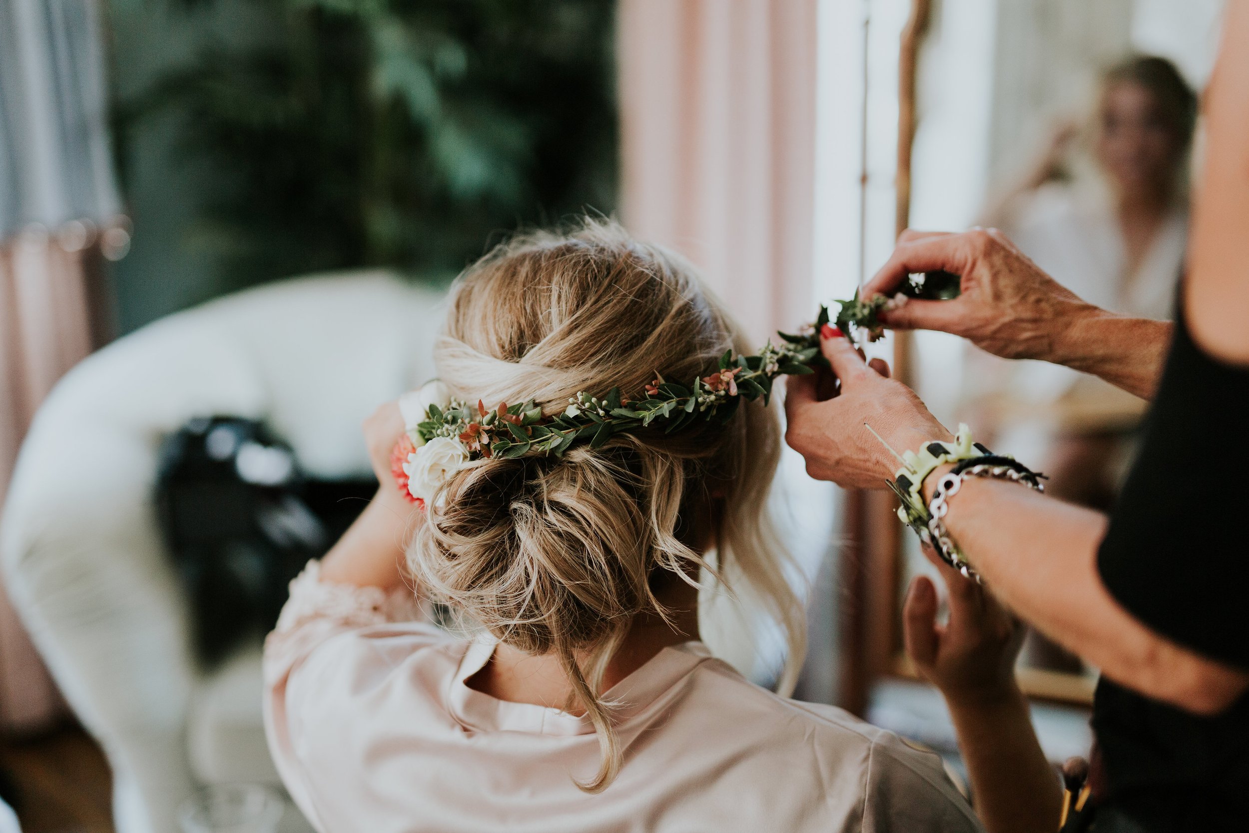 A woman wearing a floral crown has her hair styled by another woman in a dressing room – styled by One Salon & Bridal Co in St. Charles, IL