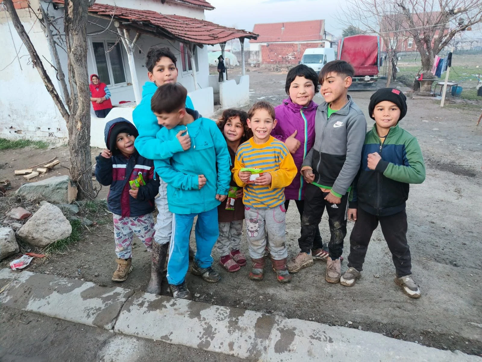 A group of children standing outdoors near a house, smiling and posing for the photo, with some holding snacks.
