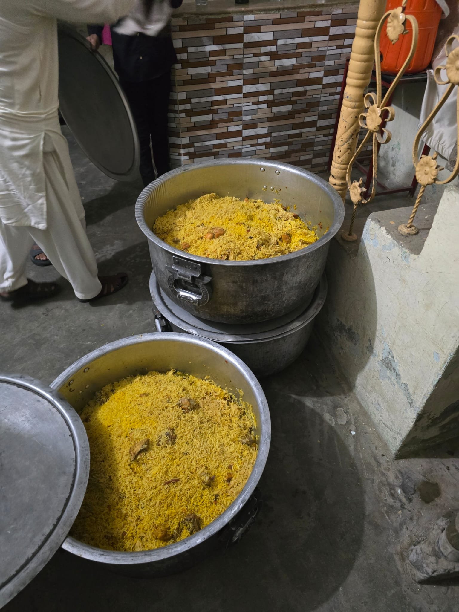 Large pots of cooked yellow rice with pieces of chicken in a kitchen setting.