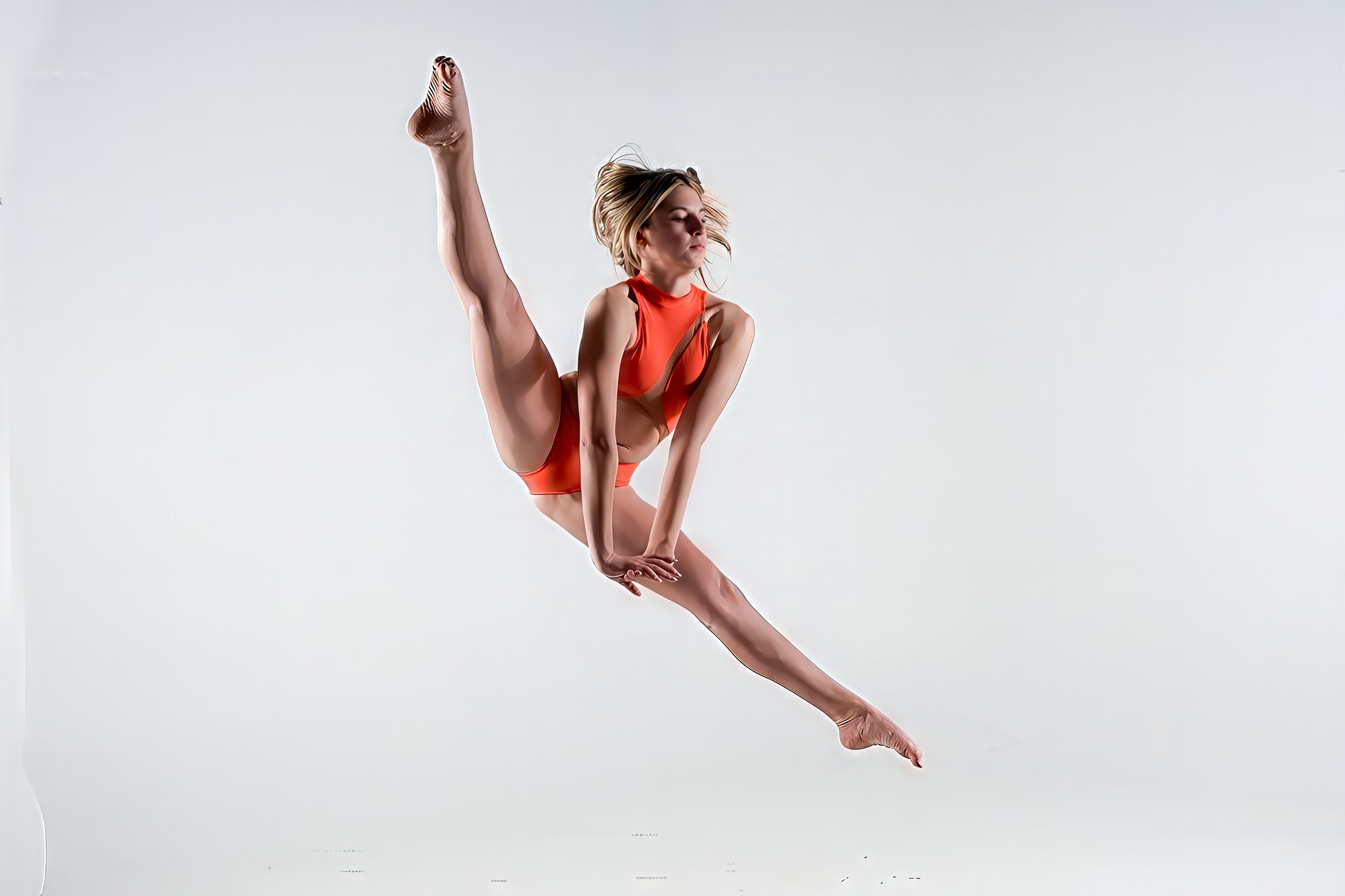 A female gymnast performing a leap in mid-air against a plain background, wearing a red competition leotard.