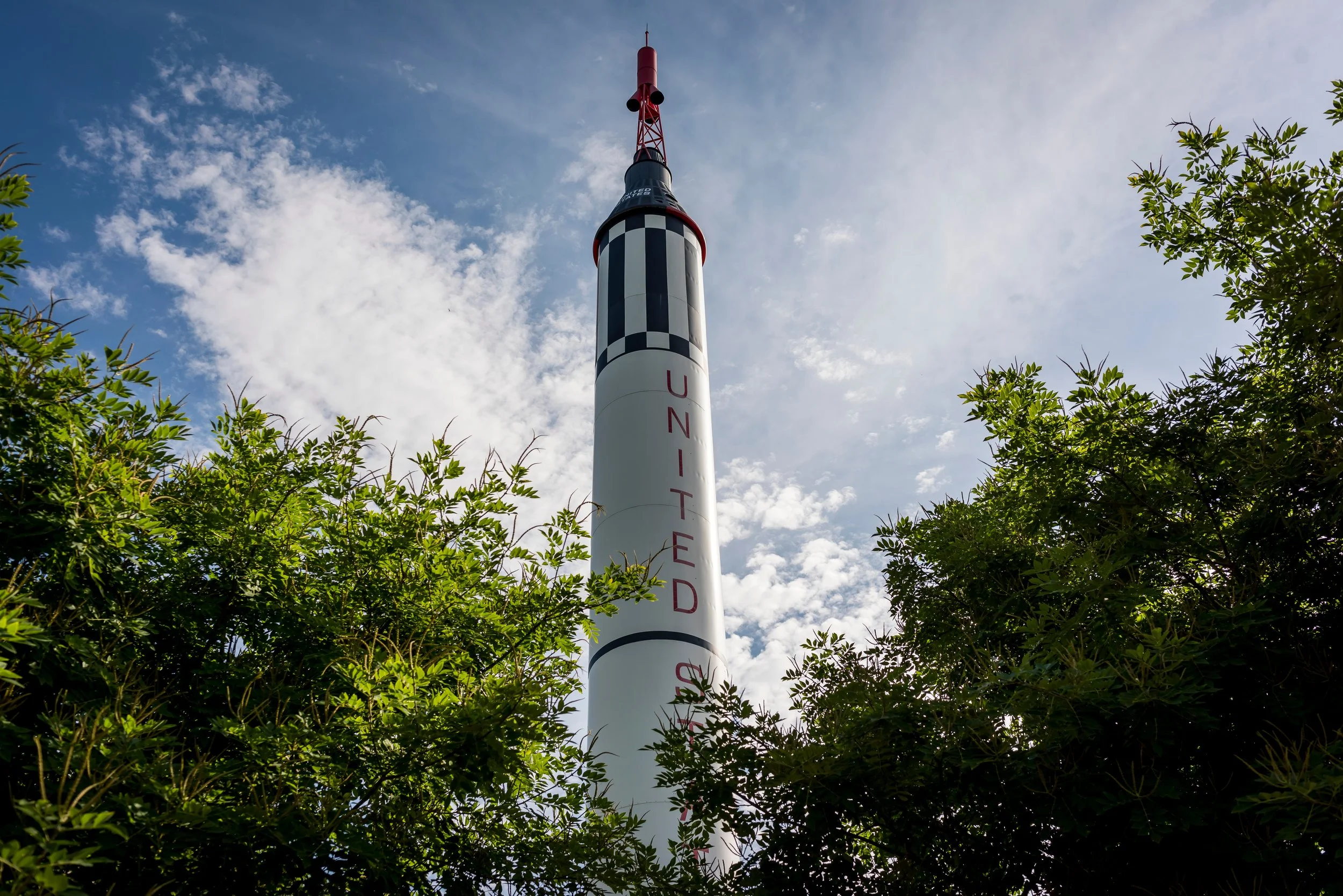 Redstone rocket replica centered in front of a cloud-filled sky surrounded by trees