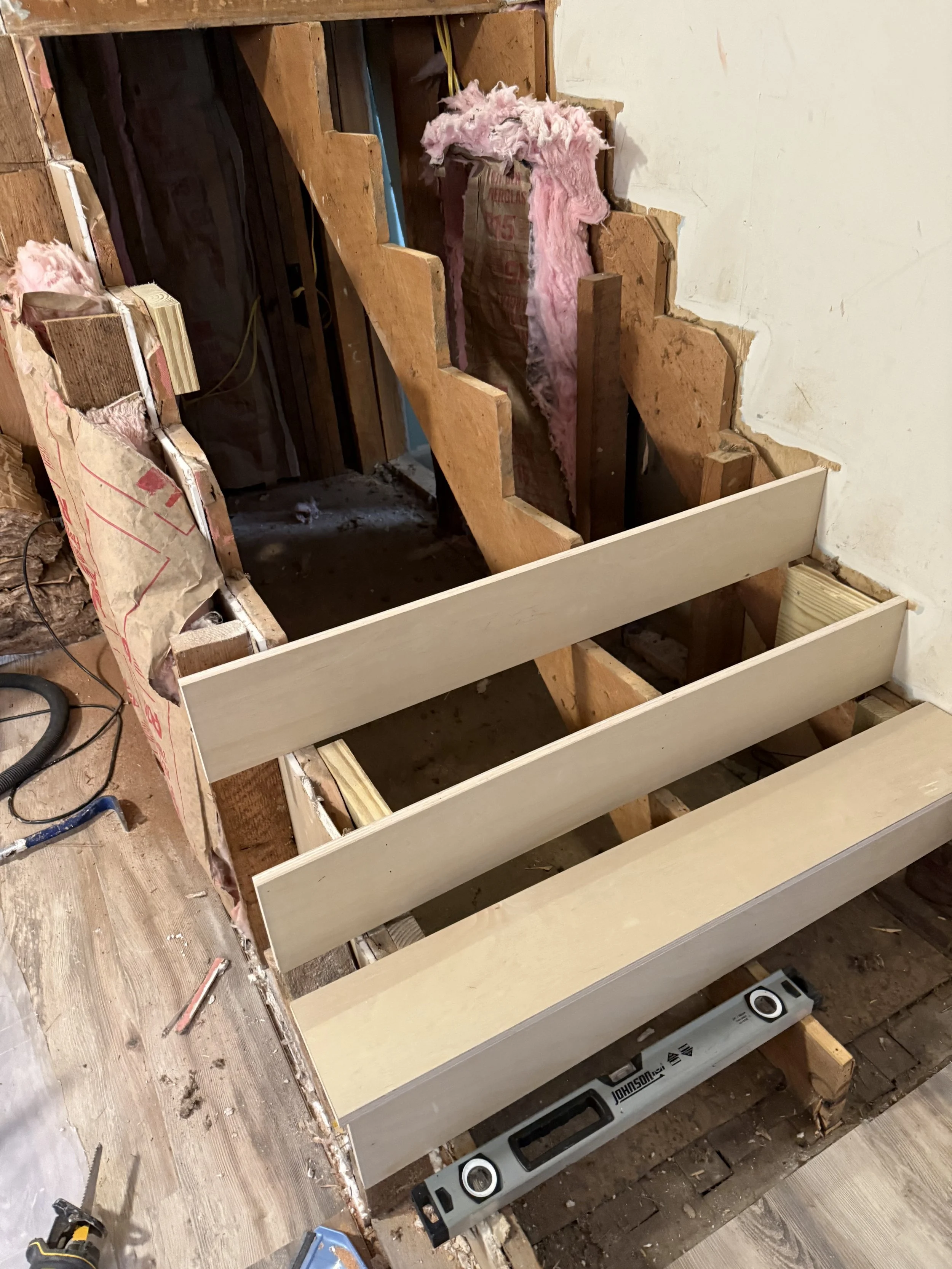 Construction site with partially built wooden staircase, insulation material, tools, and a speaker during renovation.