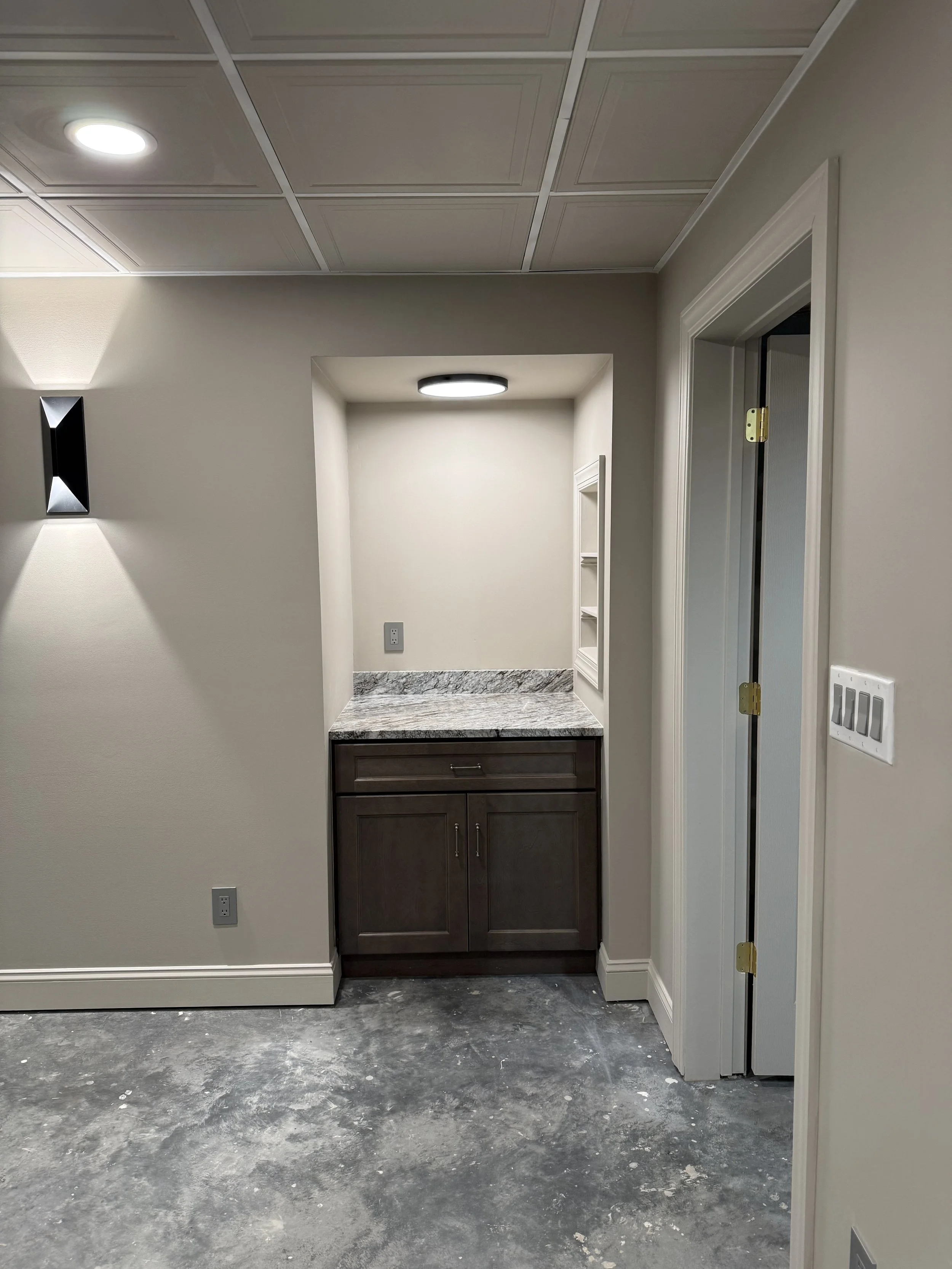 Interior of a room with newly added small built-in counter, beige walls, a light fixture, and open closet space with white shelves.