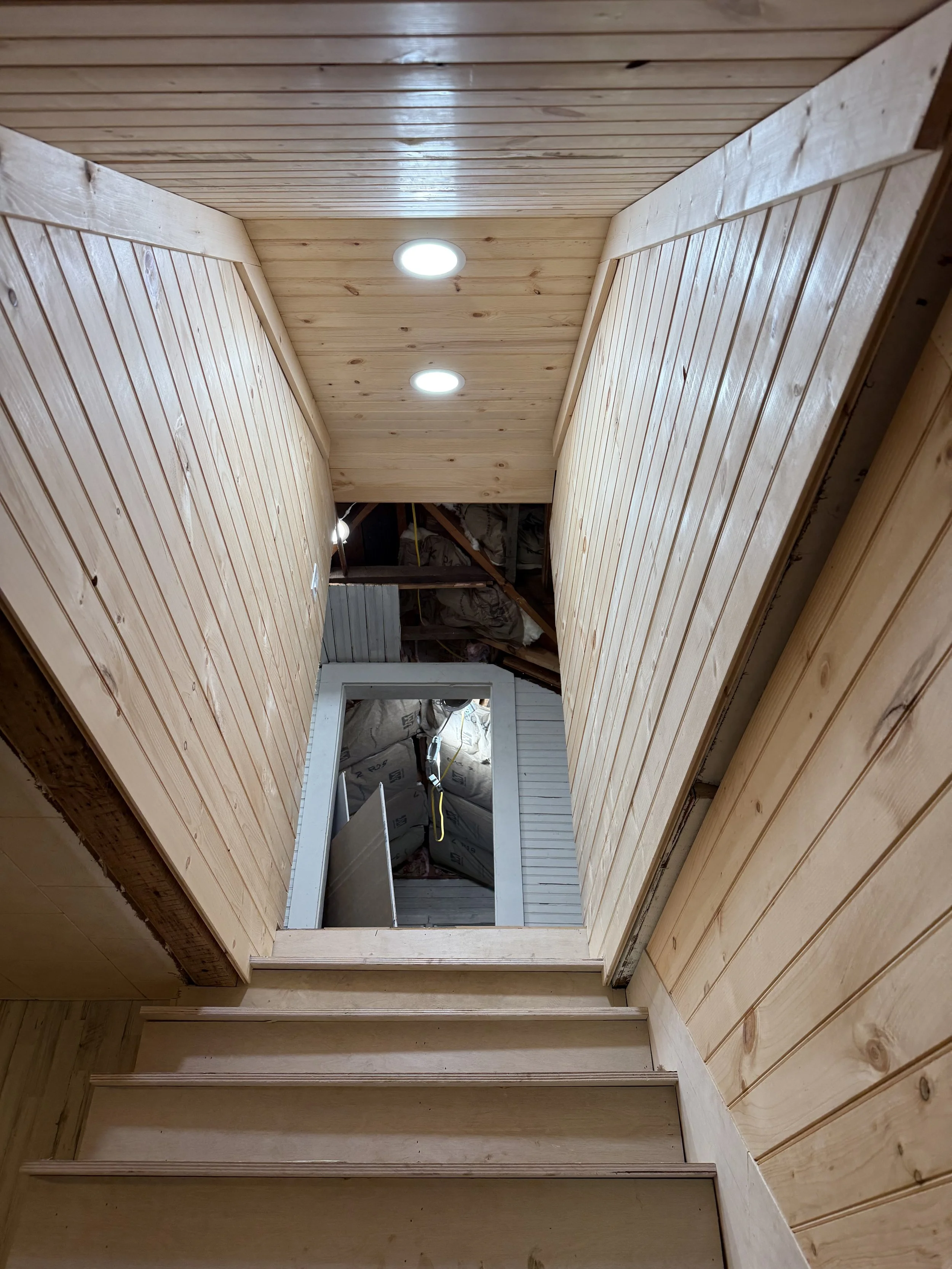 Wood-paneled interior space with recessed ceiling lights and an open doorway leading into a room under construction, showing insulation and building materials.