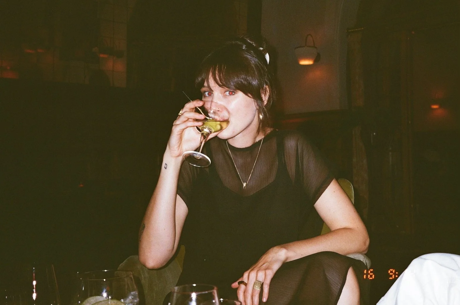 Bella Graves sitting in a dimly lit room, drinking a martini.