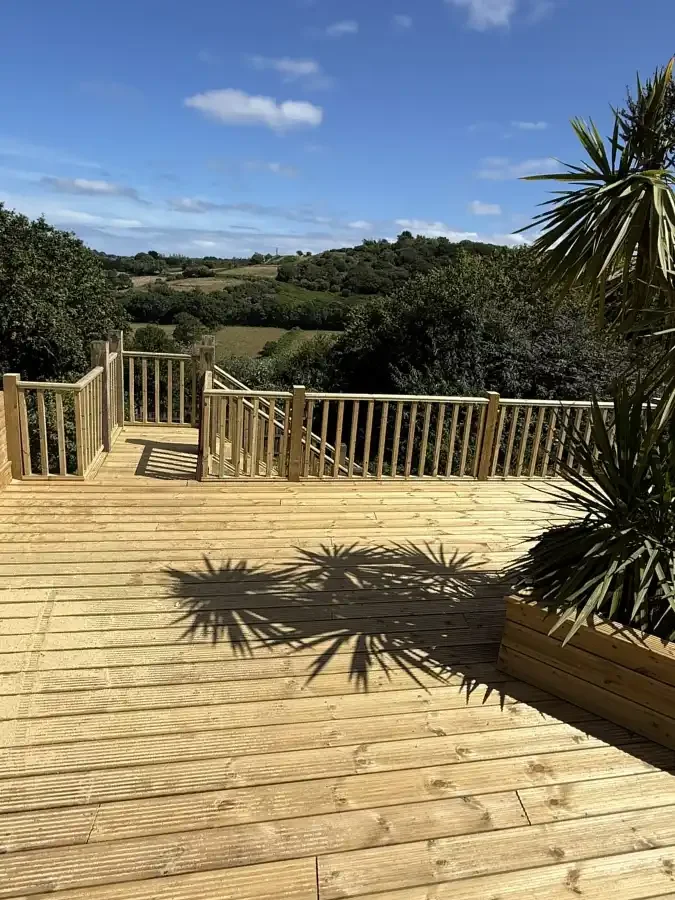 A wooden deck overlooking a green landscape with rolling hills and trees, under a clear blue sky with a few clouds.