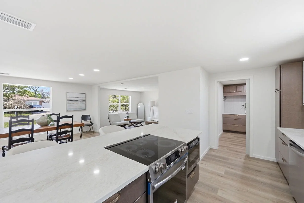 Open-concept kitchen with large island cooktop, light countertops, wood cabinetry, and adjoining dining and living areas.