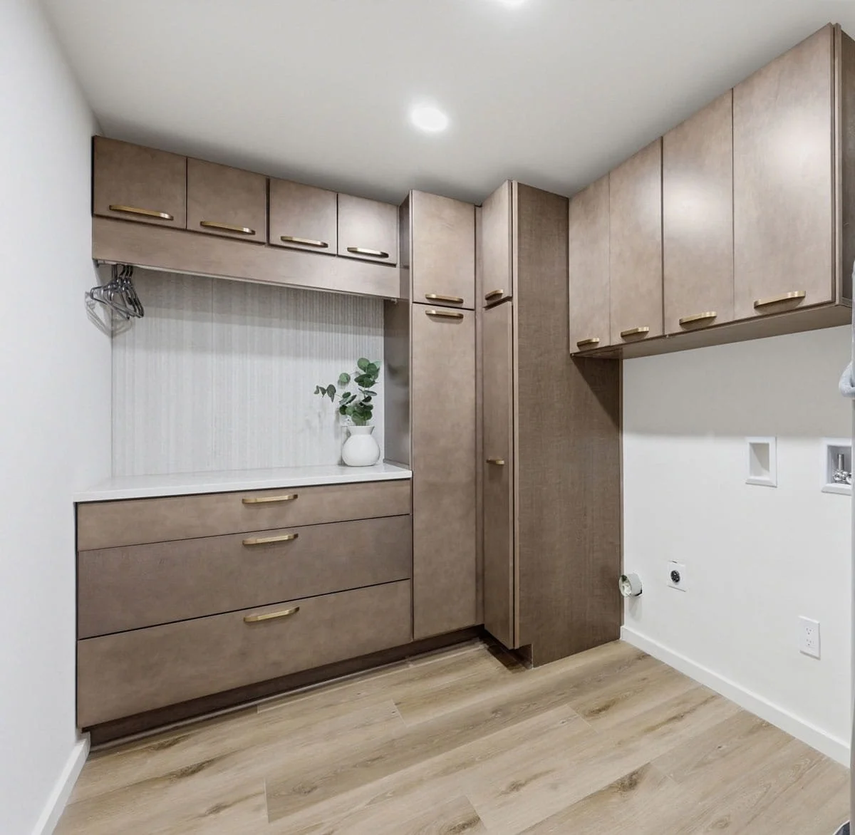Custom laundry room with warm wood cabinetry, brass hardware, built-in hanging space, and countertop with storage drawers.