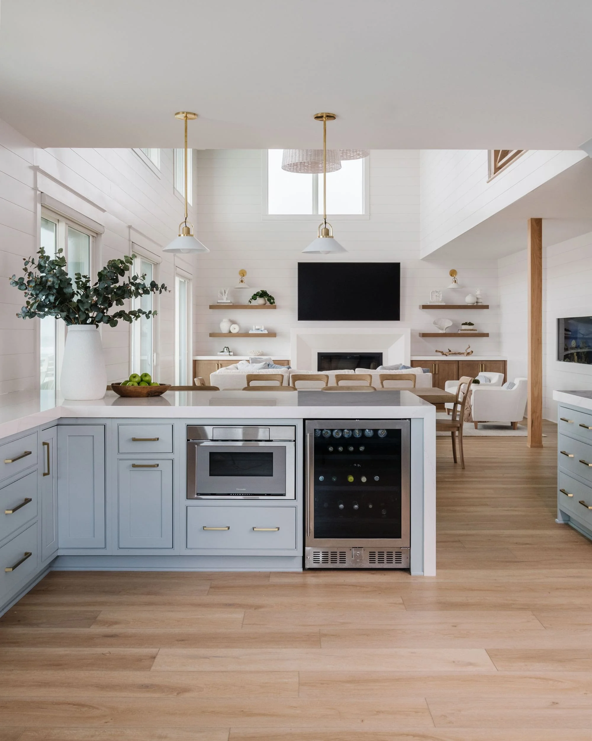 Open-concept kitchen and living room with blue cabinets, white quartz counters, light wood floors, and built-in microwave and beverage fridge.
