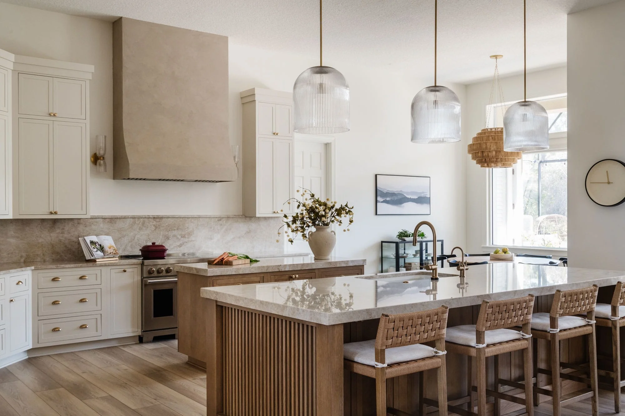 Spacious modern kitchen with beige cabinets, a large island with a quartz countertop, hanging pendant lights, and a view of the dining area with chairs and windows.