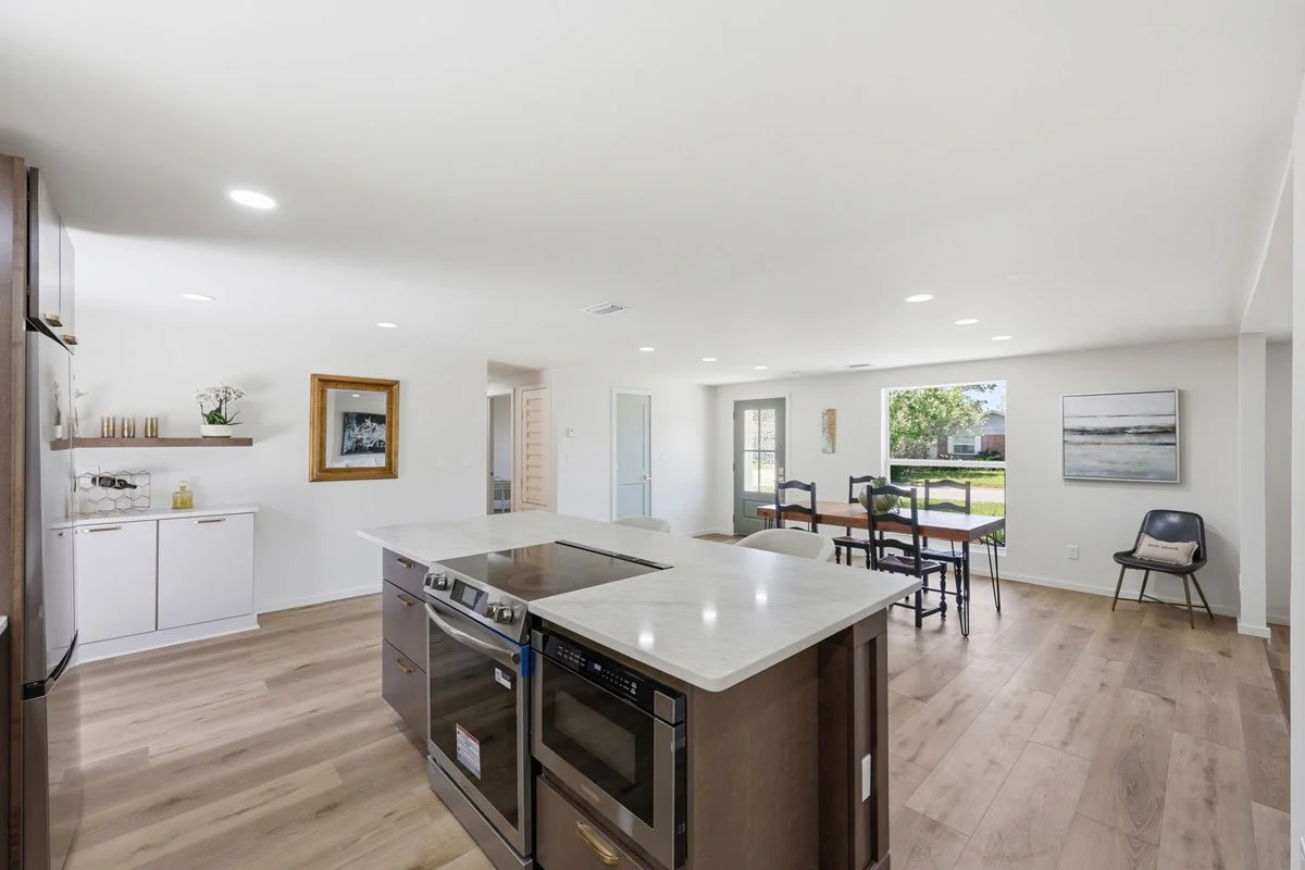 Open-concept kitchen and dining area with large island cooktop, light countertops, wood cabinetry, and light wood flooring.