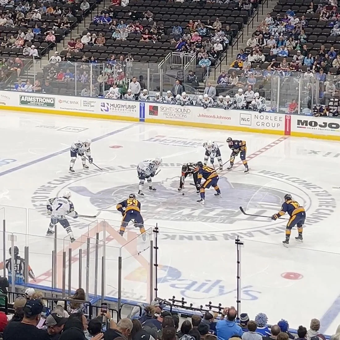 Ice hockey game at VyStar Veterans Memorial Arena with players facing off at center ice and fans in the stands.