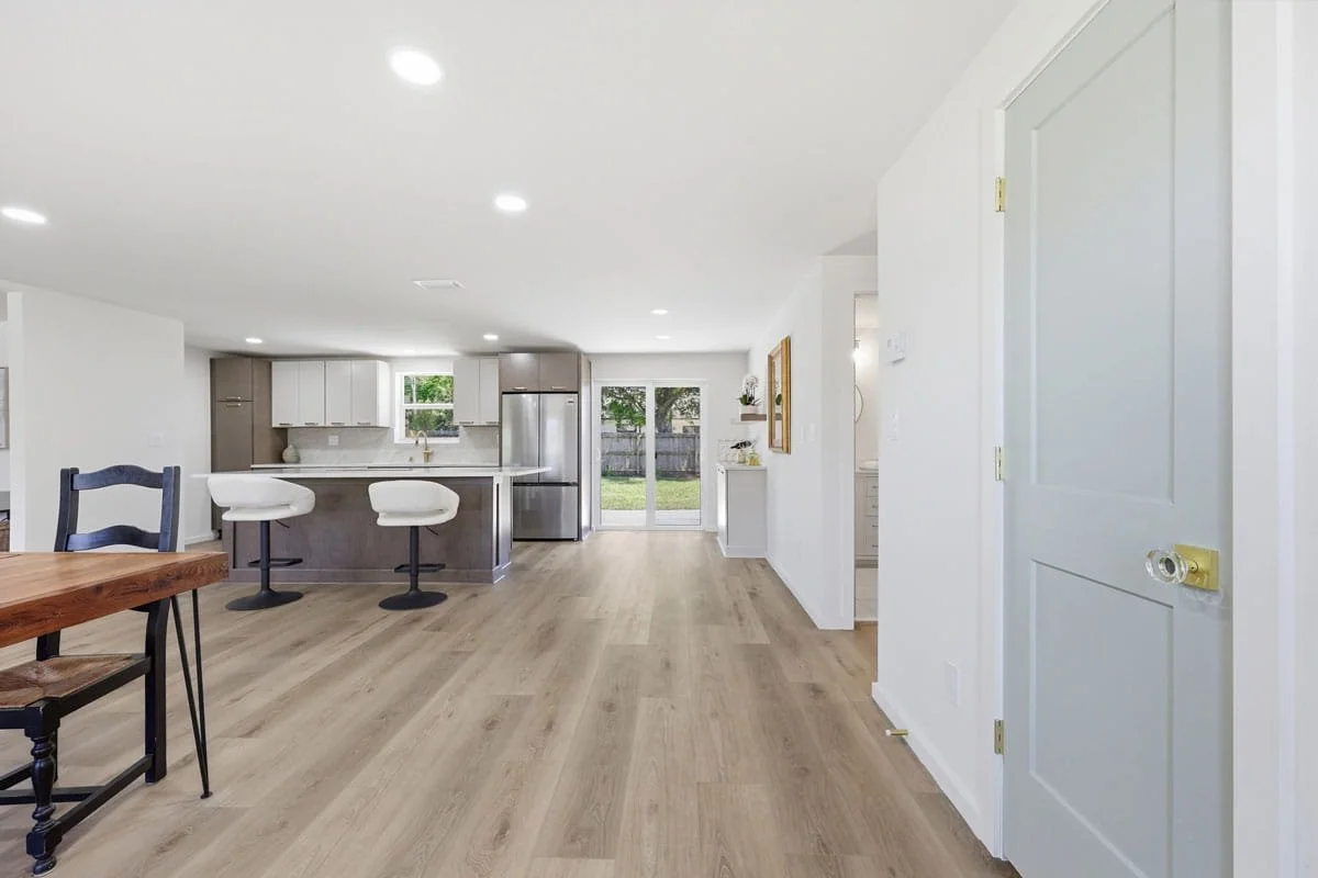 Open-concept kitchen and dining area with large island, white and wood cabinetry, bar stools, and sliding glass doors leading to the backyard.