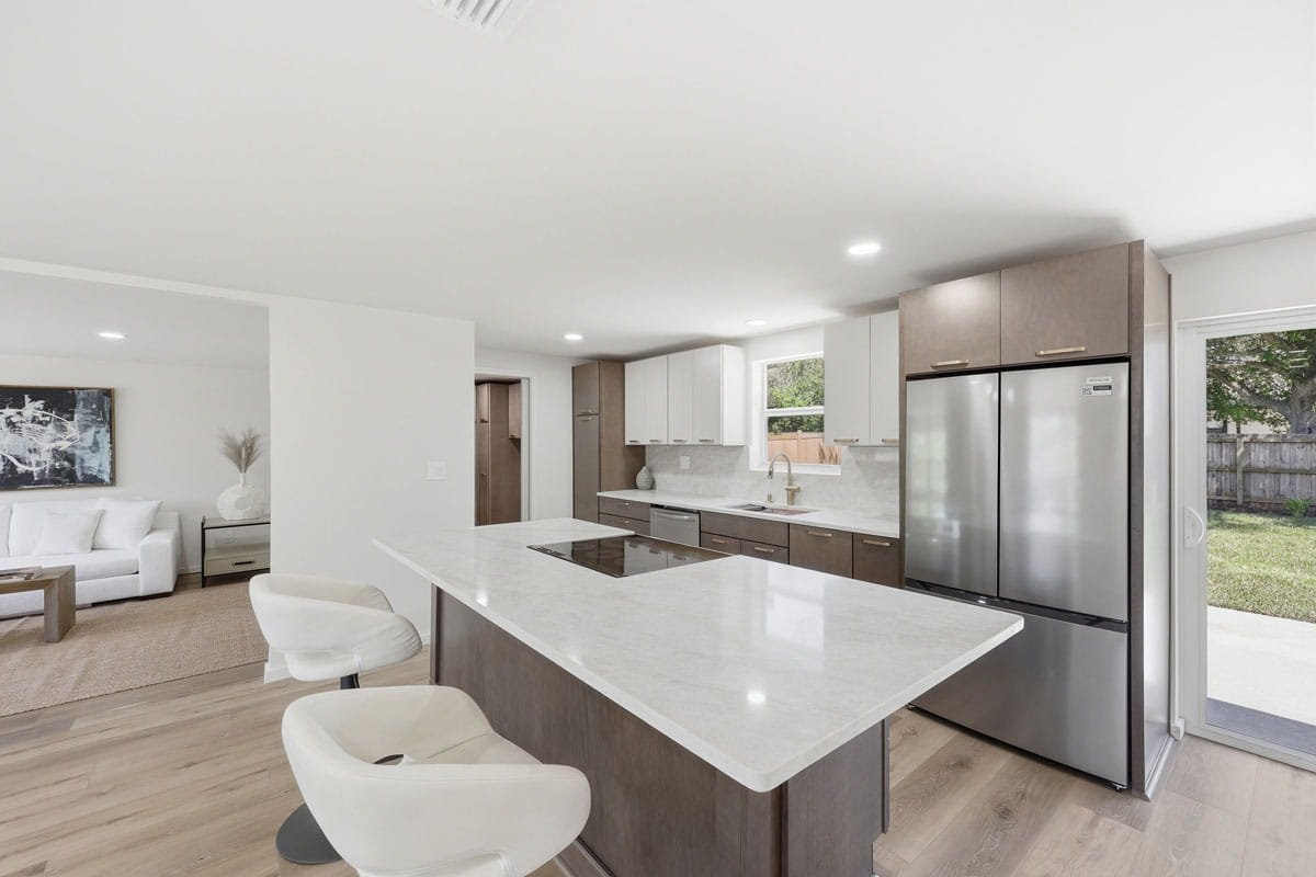 Modern kitchen with light countertops, wood cabinetry, stainless steel refrigerator, and large island with seating.