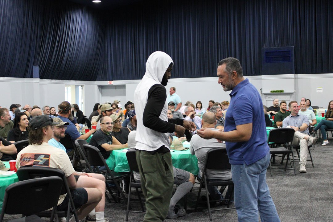 A Woodsman employee receives a raffle prize during the annual ESOP Breakfast as coworkers watch and celebrate from tables throughout the room.