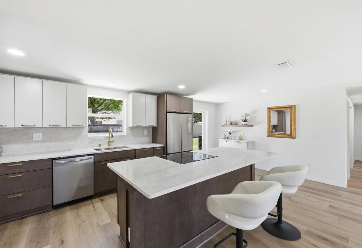 Modern kitchen with large island, light countertops, wood cabinetry, stainless steel appliances, and bar seating.
