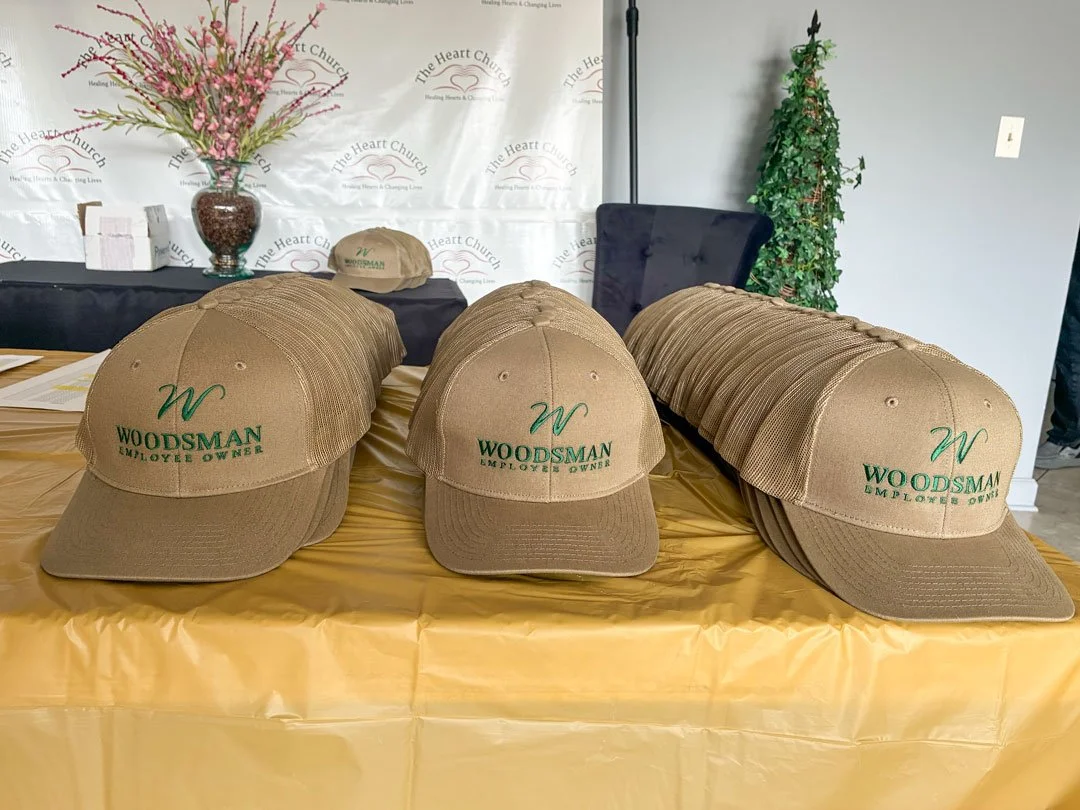 Rows of tan Woodsman Employee Owner hats displayed on a table before the company's annual ESOP Breakfast, ready for employee-owners to receive as commemorative gifts.