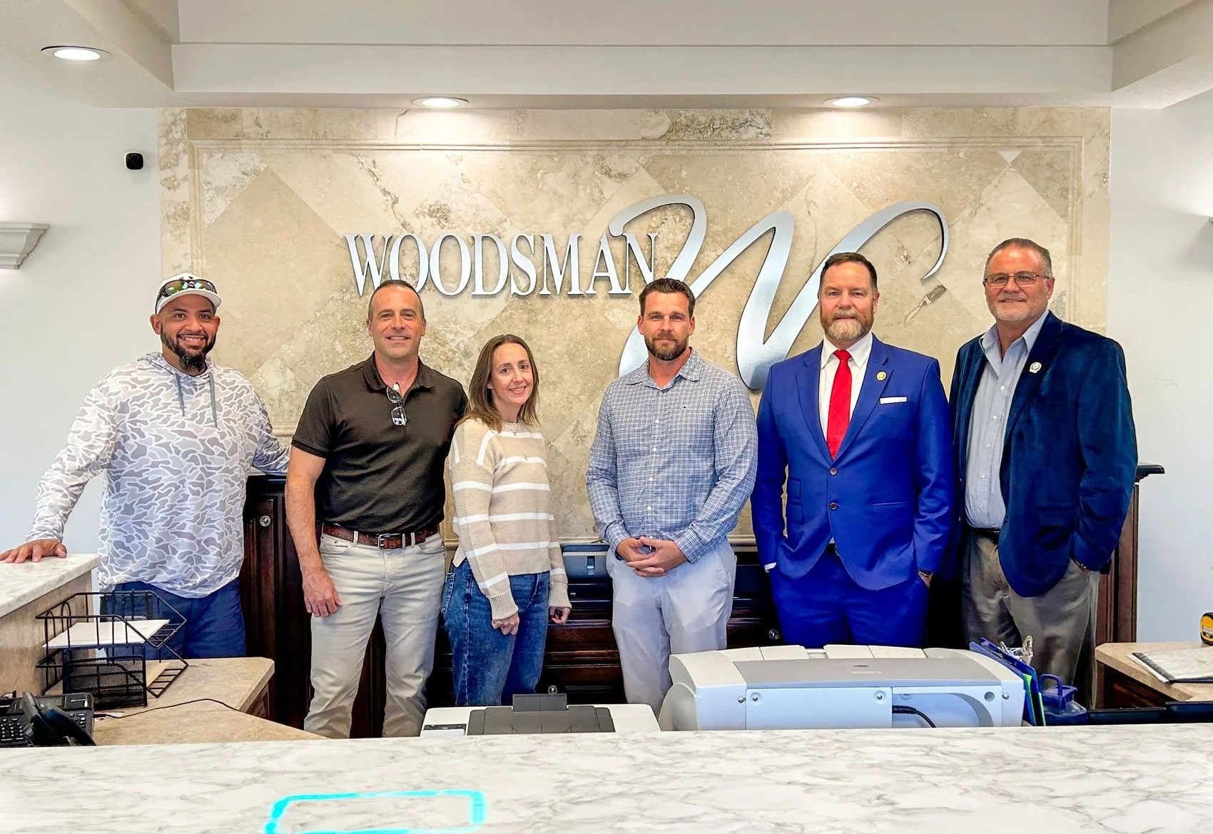Congressman Aaron Bean standing in front of the Woodsman Logo with Woodsman employee owners.