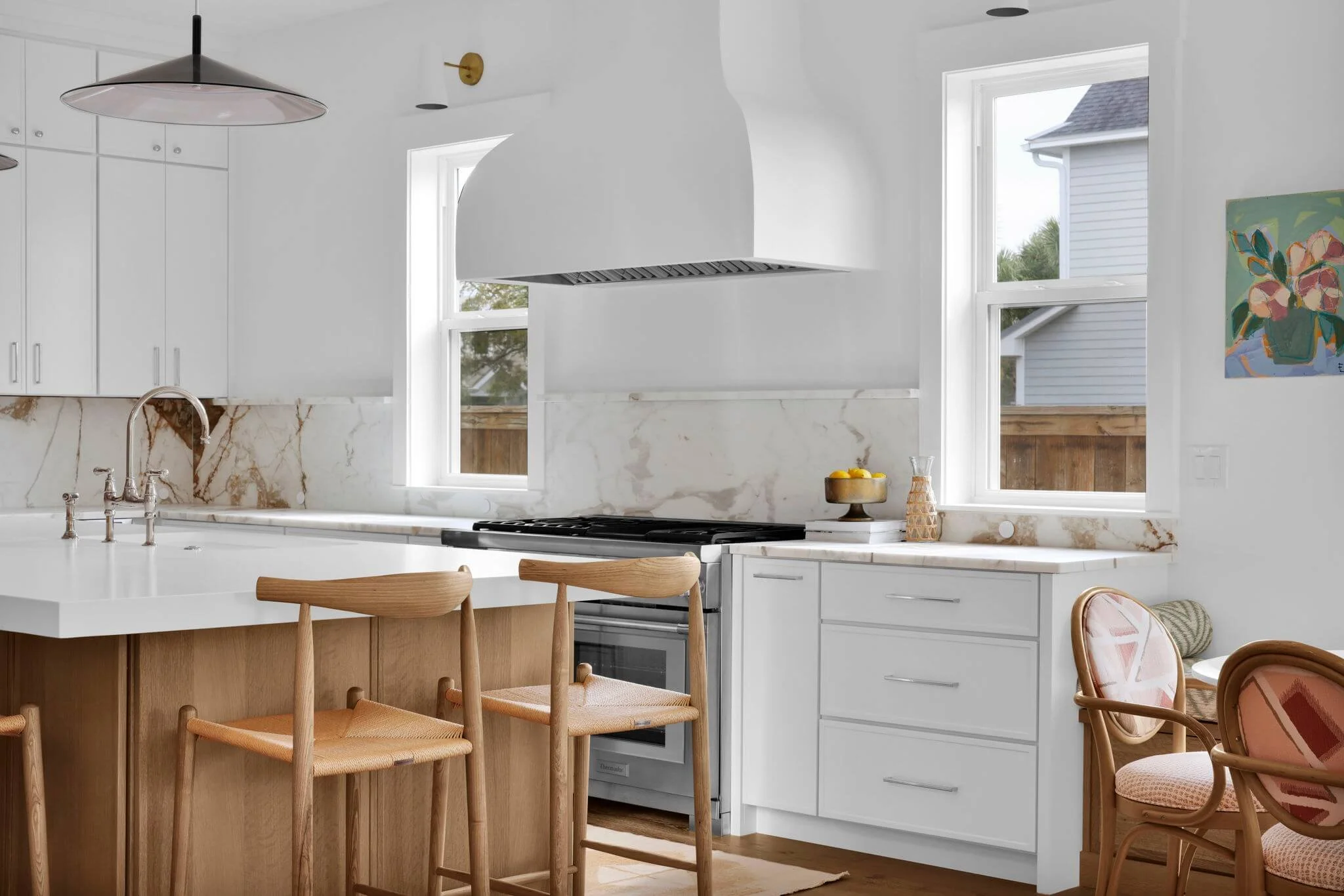 Bright kitchen with white cabinets, wood island, marble-look backsplash, and a sculptural white range hood between two windows.