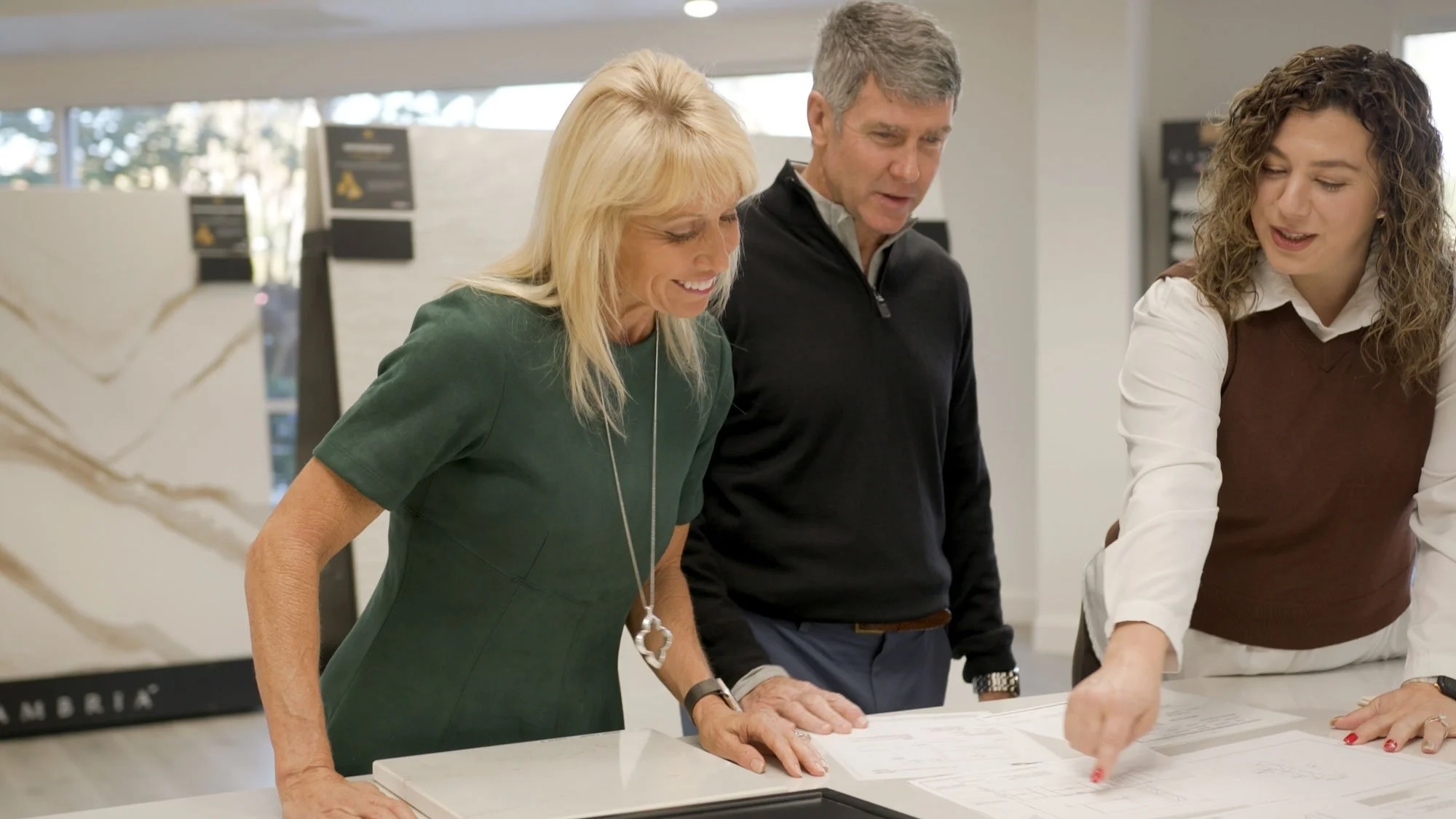 Kitchen designer reviewing plans with a couple in a showroom, pointing out details on cabinetry and layout selections.