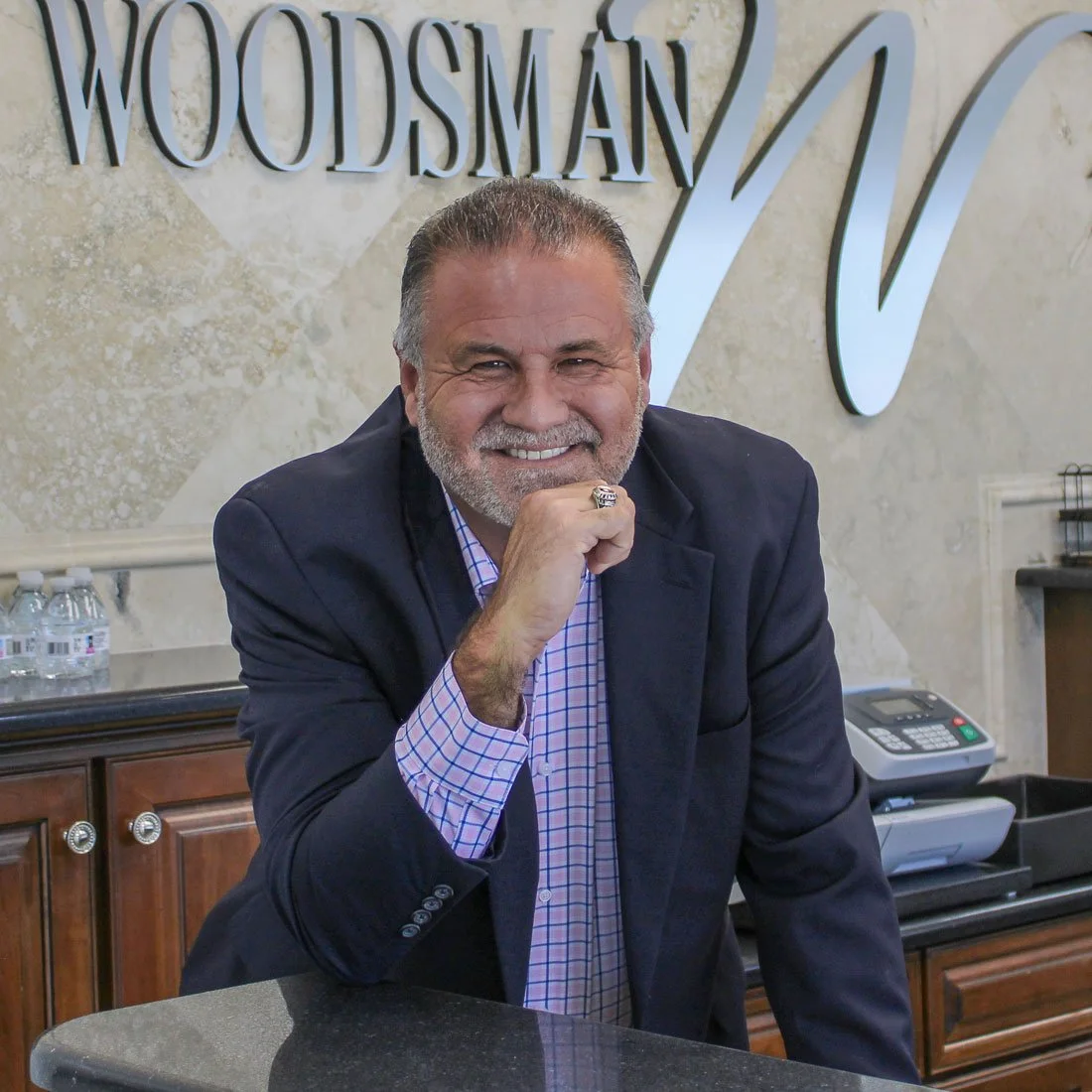 Brad Mangold, president of Woodsman Kitchens & Floors, smiling at the showroom counter with company signage in the background.