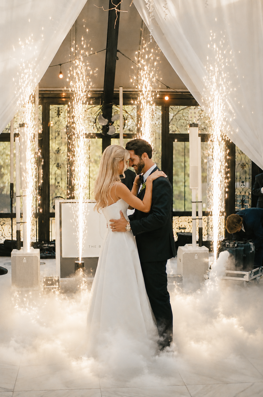 A bride and groom sharing their first dance at their wedding reception at Edinburgh West in Greenville, SC, surrounded by cold spark fountains, and our dancing on the clouds effects