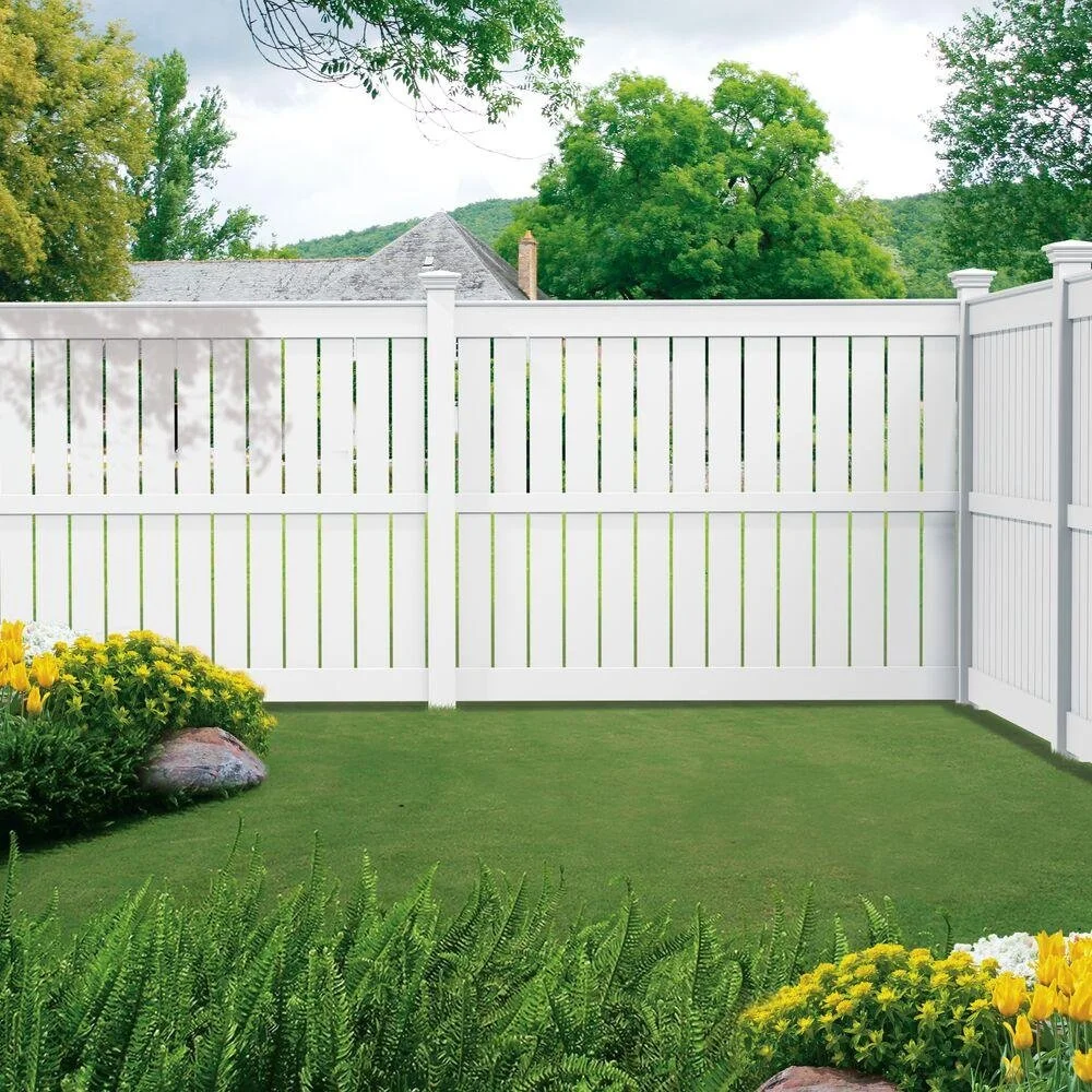 White vinyl privacy fence in a backyard with green grass, yellow flowers, and trees in the background.
