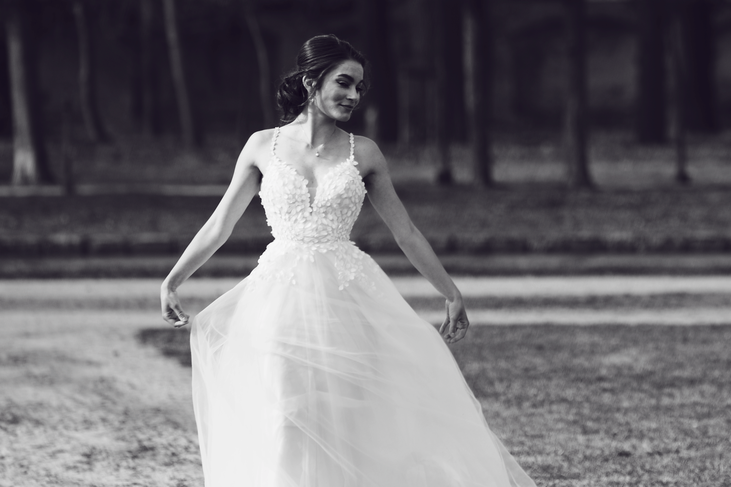 Black and white photo of a woman in a wedding dress twirling outdoors.