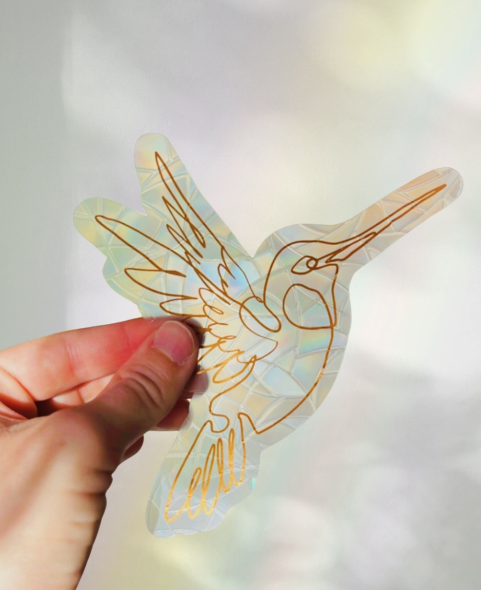 A person holds a colorful paper cutout of a hummingbird against a neutral background.
