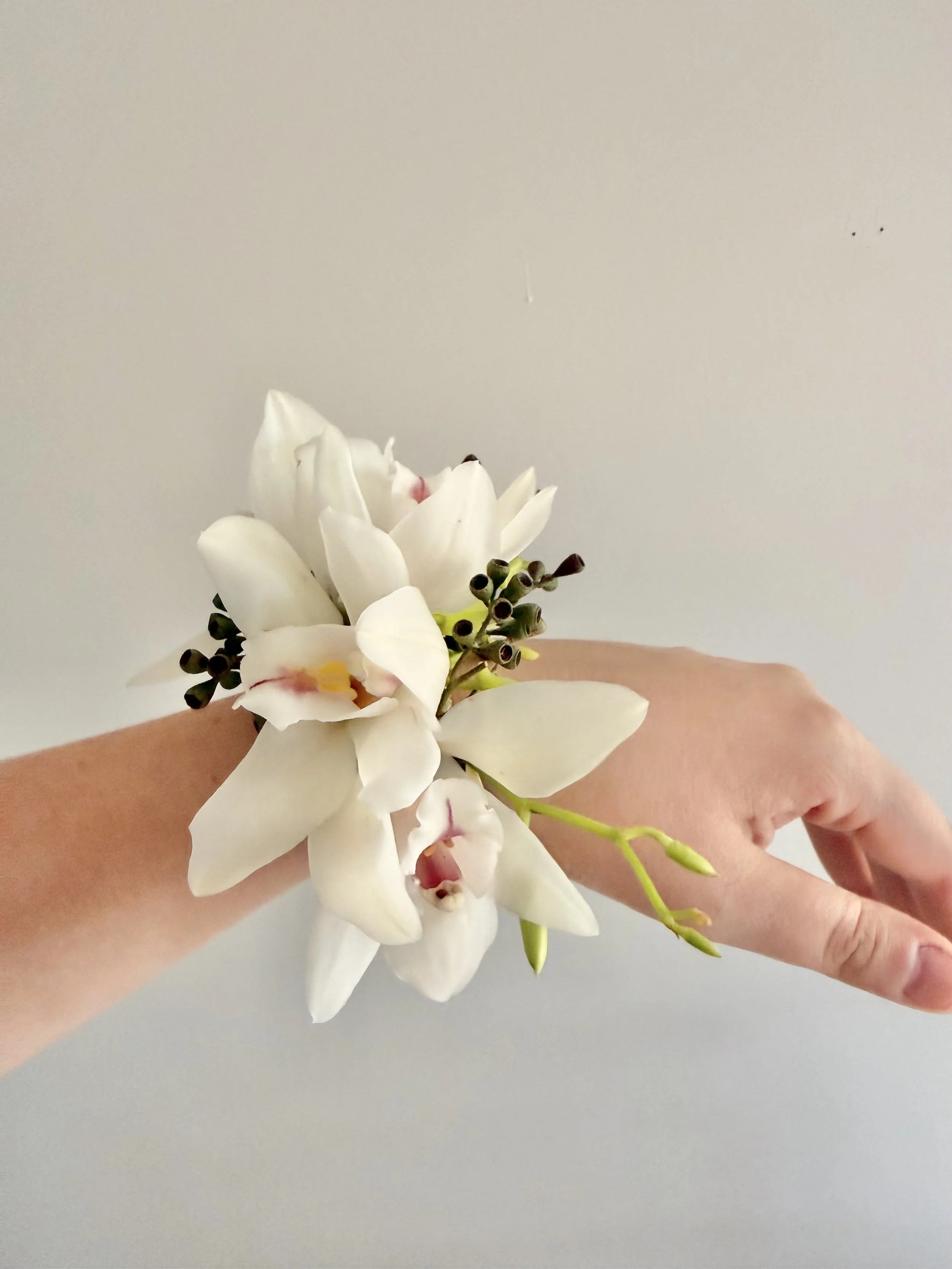 A hand holding a small bouquet of white orchids and dark berries against a plain light gray background.