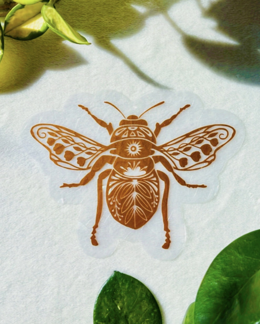 A colorful bee sticker placed on a clean white surface, showcasing its detailed design and vibrant colors.