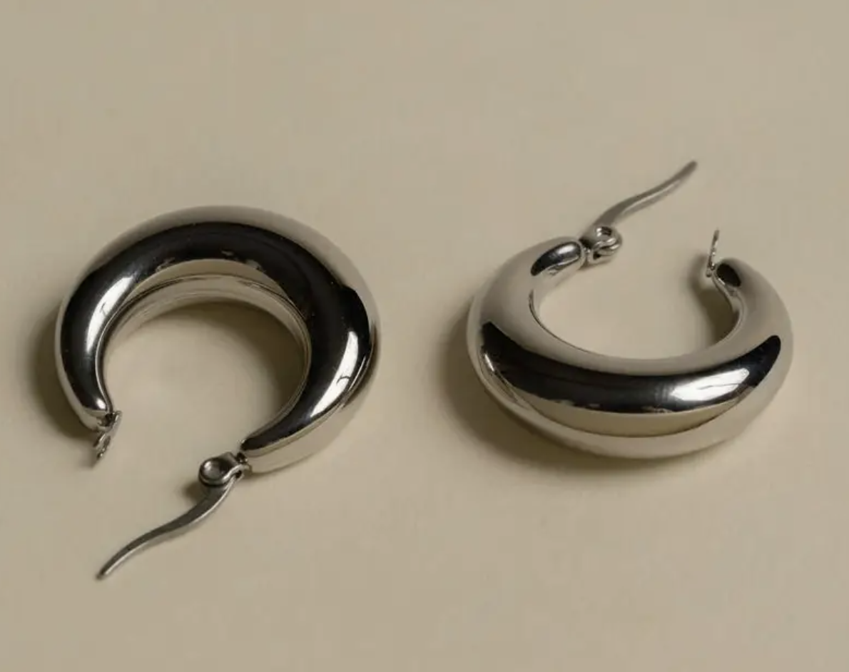 Two silver hoop earrings resting on a white surface, showcasing their shiny finish and circular design.