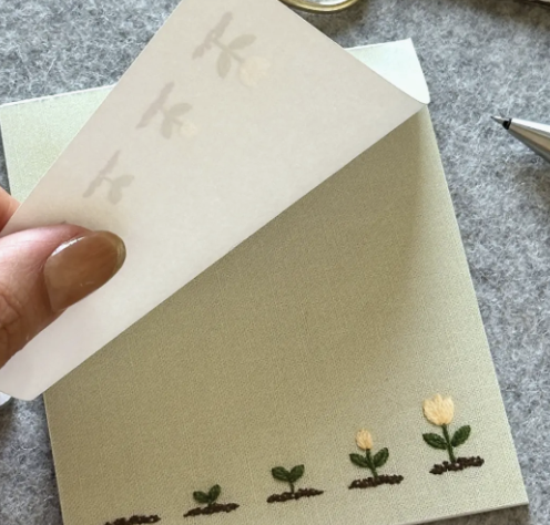 A person is carefully cutting out a floral card with scissors, focusing on the intricate flower designs.