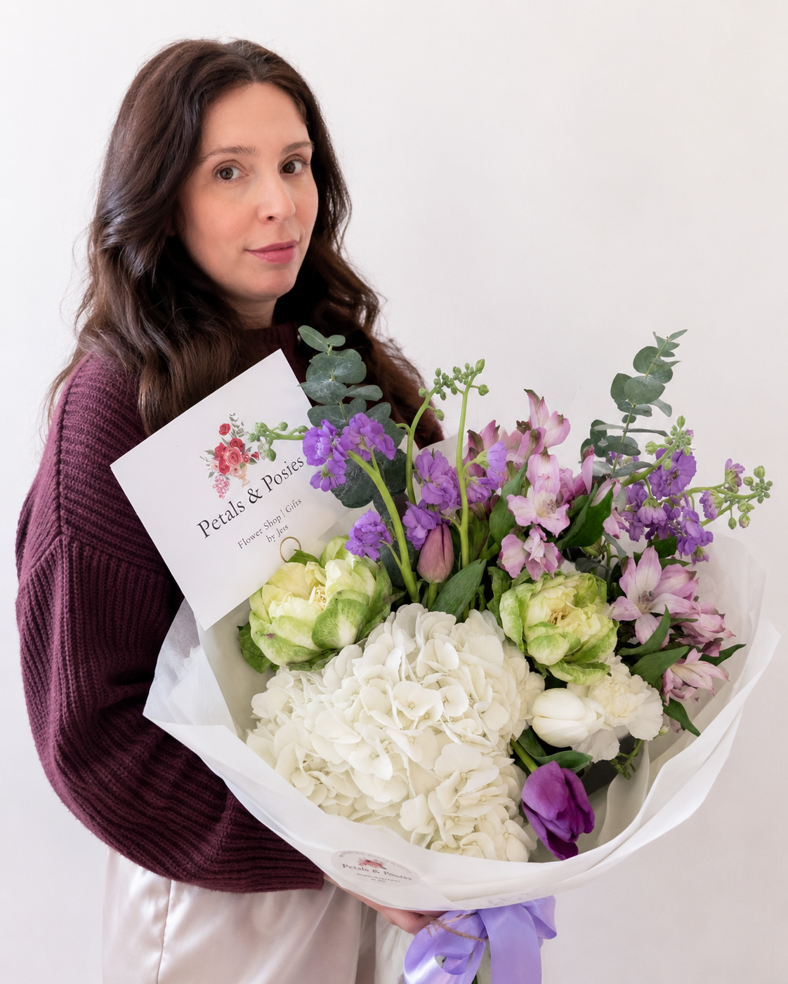 Woman holding a large bouquet of mixed flowers with a sign reading 'Petals & Posies Flower Shop Gifts'
