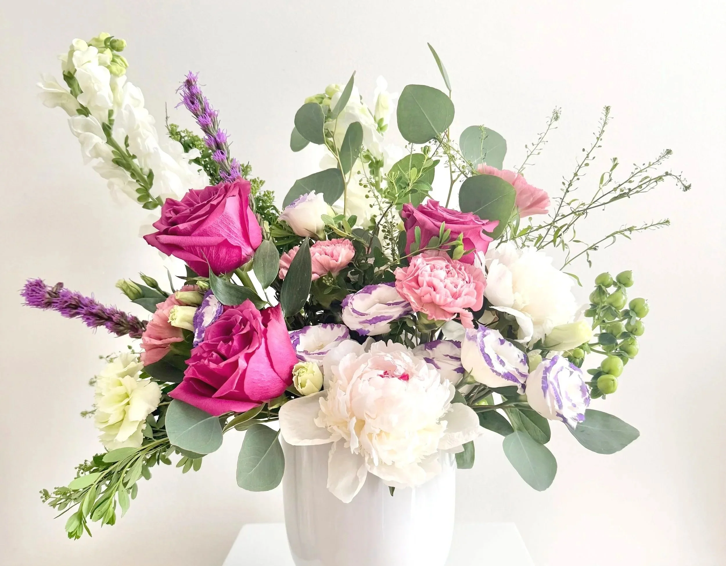 A bouquet of assorted pink, white, purple, and green flowers and greenery on a light background.