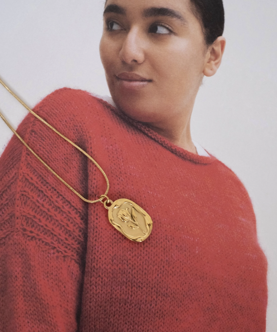 A woman wears a gold necklace featuring a pendant with a photo of a person, highlighting a personal connection.