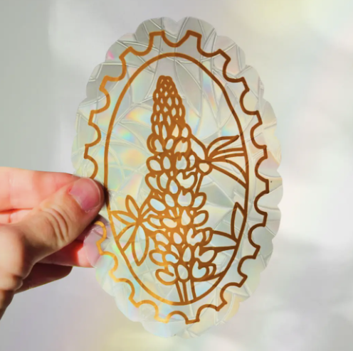A person holds a colorful flower sticker, showcasing a vibrant design against a neutral background.