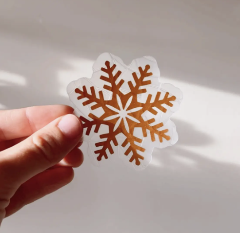 A person holding a small sticker shaped like a snowflake, showcasing intricate details and a light blue color.
