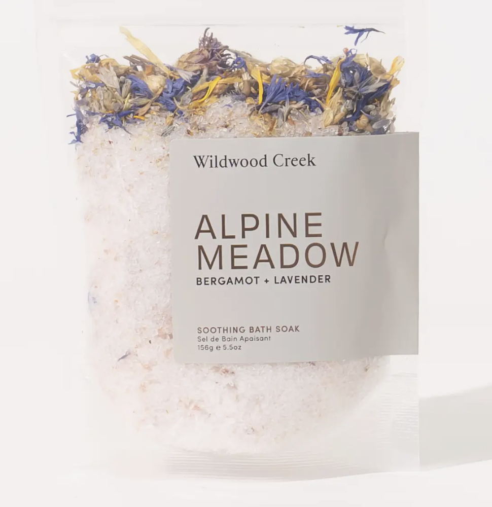 Bath salts labeled "Wildwood Creek Alpine Meadow," featuring a serene alpine meadow design on the packaging.