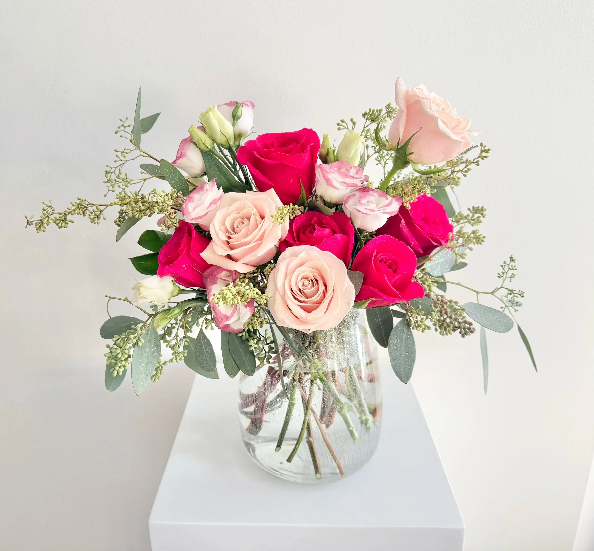 A vase filled with vibrant pink and red roses, showcasing their lush petals and green foliage.