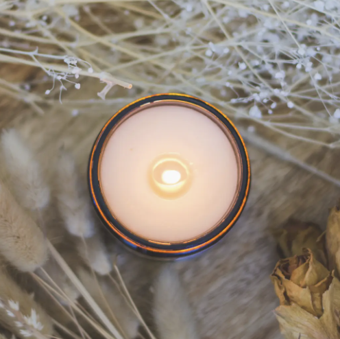 A candle placed on a wooden table surrounded by dried grass, creating a warm and rustic atmosphere.