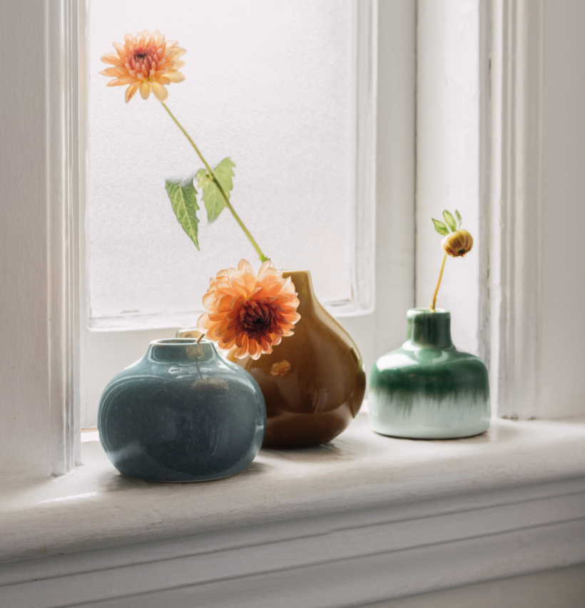Three vases filled with colorful flowers are arranged on a sunlit window sill.