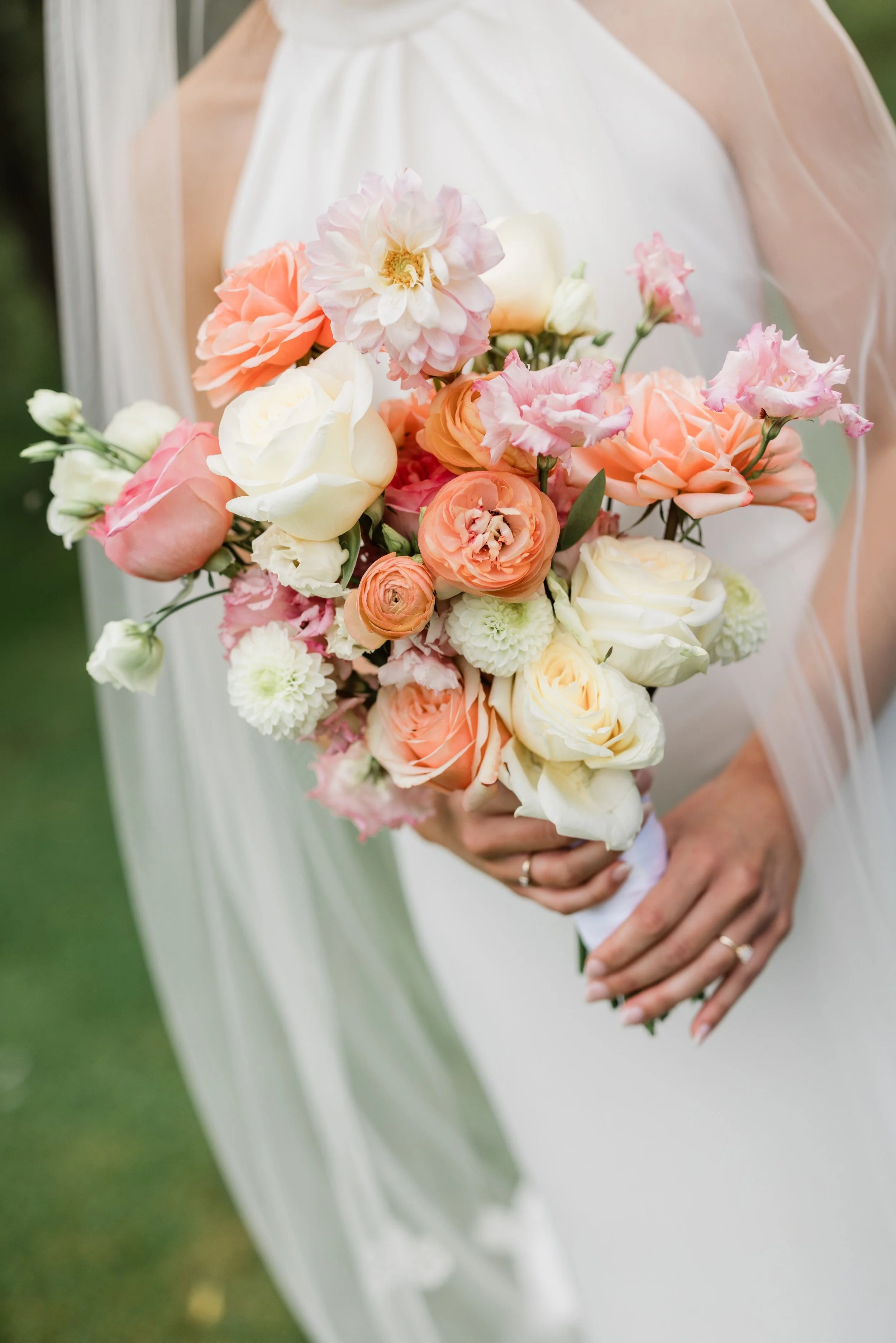 Close-up of a bride holding a bouquet of pink, white, and peach roses and other flowers.