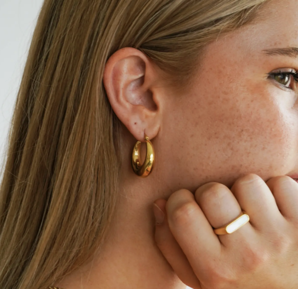 A woman with gold hoop earrings and a ring, showcasing her elegant jewelry style.