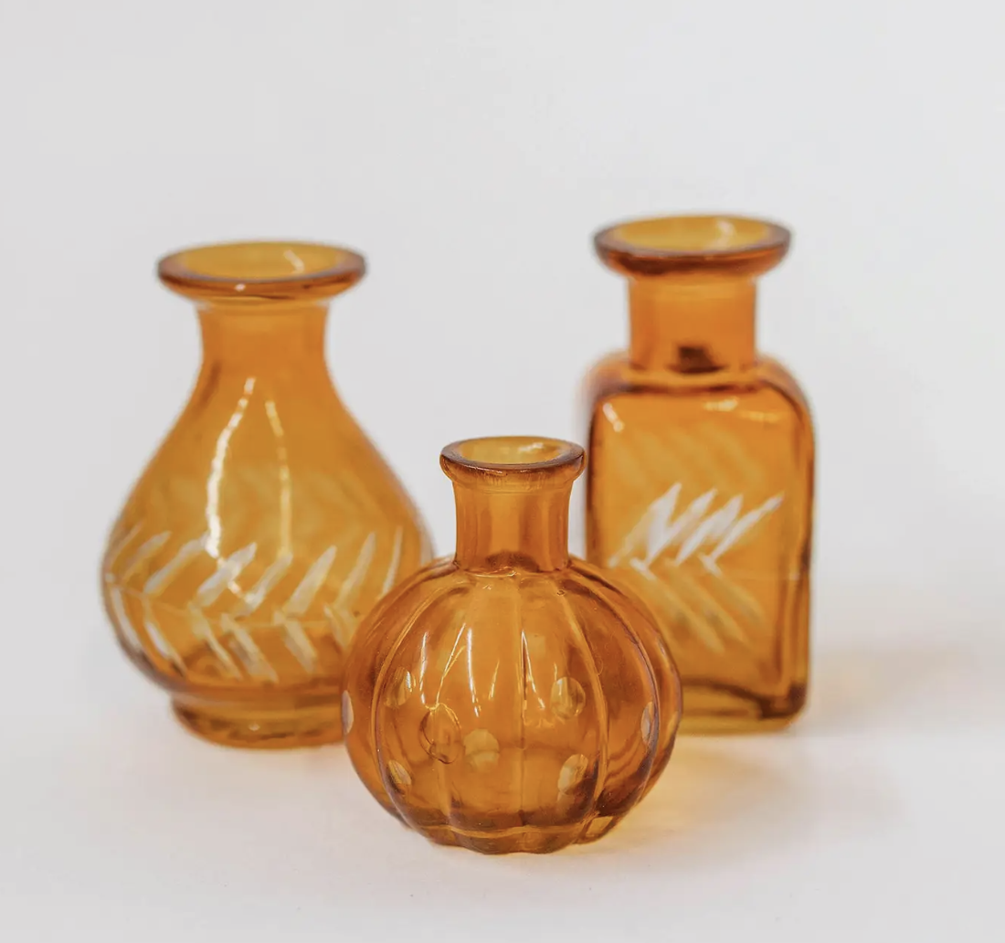 Three small glass vases featuring intricate designs, arranged closely together on a neutral background.