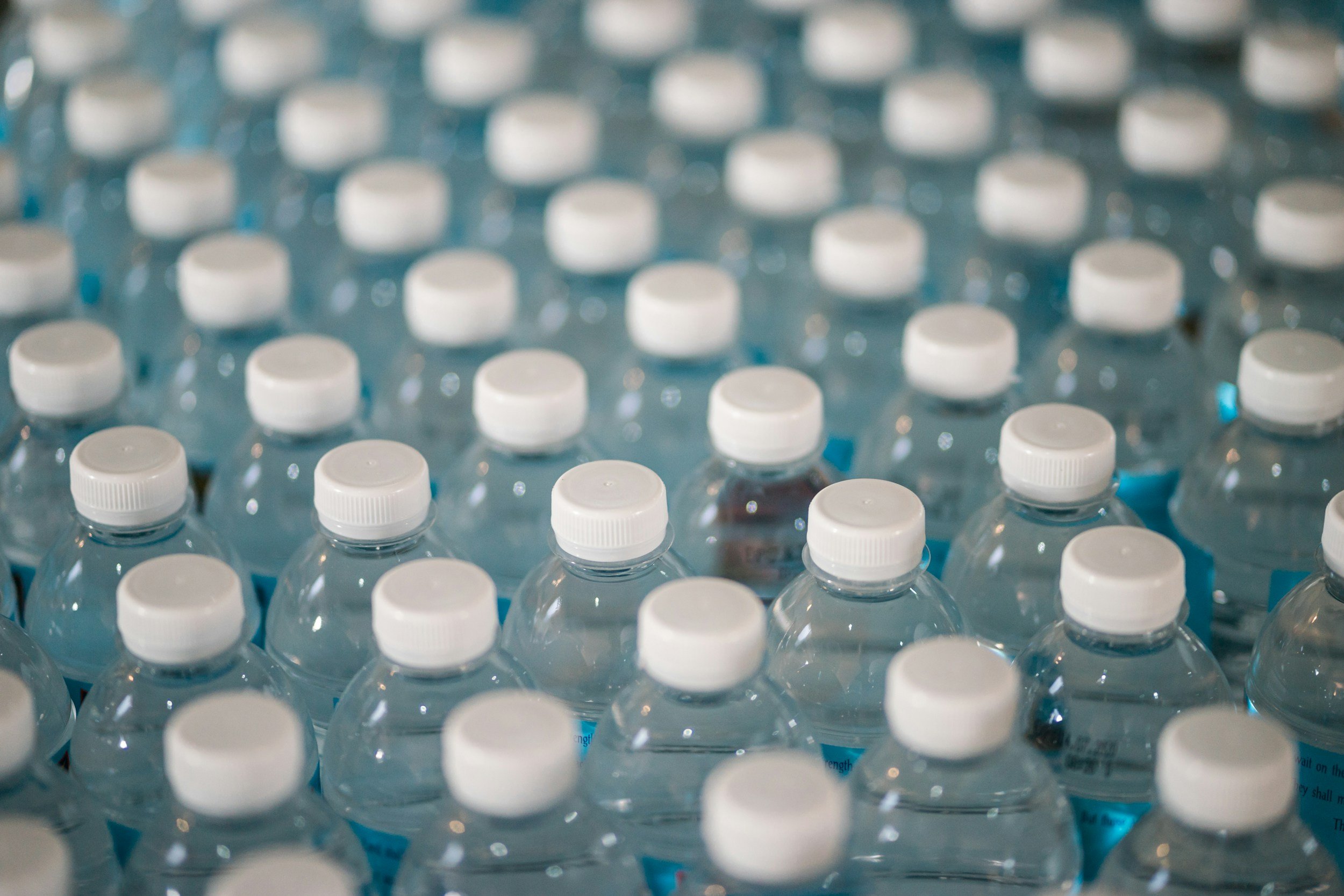 Multiple rows of clear plastic water bottles with white caps, arranged in a factory or storage setting.