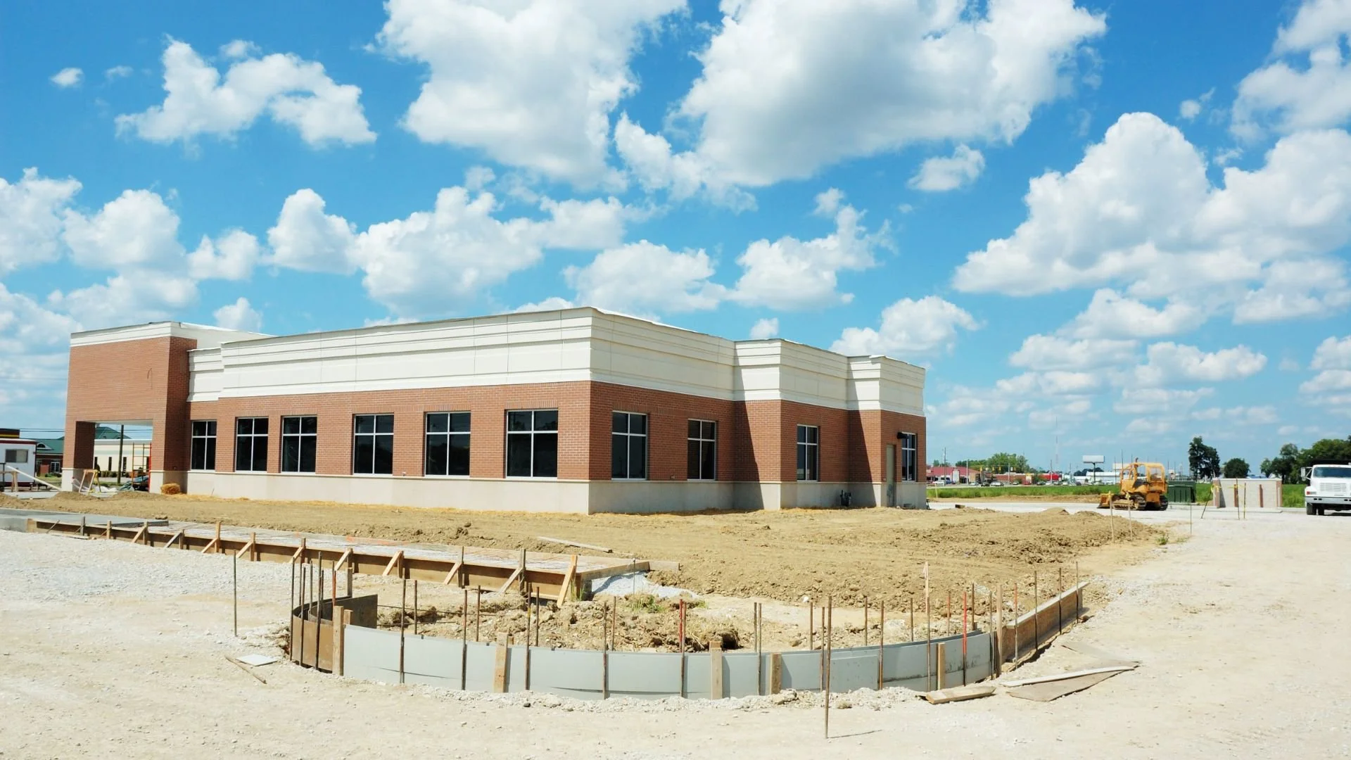 Construction site with a building under development, dirt ground, construction equipment, and a partly cloudy sky.